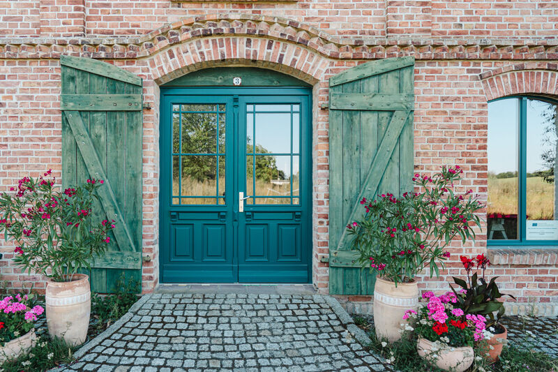 Grüne Eingangstür mit Fensterläden und Blumentöpfen